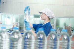 joven contento mujer trabajador en fábrica comprobación agua galones antes de envío. foto