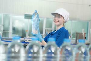 joven contento mujer trabajador en fábrica comprobación agua galones antes de envío. foto