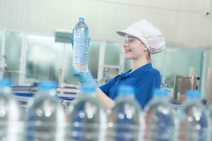 joven contento mujer trabajador en fábrica comprobación agua galones antes de envío. foto