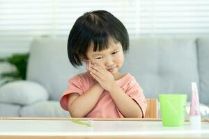 little asian girl presses hand to cheek, suffers from pain in tooth. Teeth decay, dental problems, child emotions and facial expression, oral health care, reducing sweets, fluorine coating photo