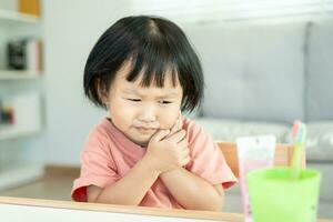 little asian girl presses hand to cheek, suffers from pain in tooth. Teeth decay, dental problems, child emotions and facial expression, oral health care, reducing sweets, fluorine coating photo