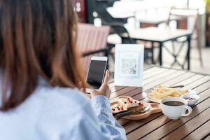 la mujer usa un teléfono inteligente para escanear el código qr para pagar en un café restaurante con un pago digital sin efectivo. elige menú y ordena acumula descuento. billetera electrónica, tecnología, pago en línea, tarjeta de crédito, aplicación bancaria. foto