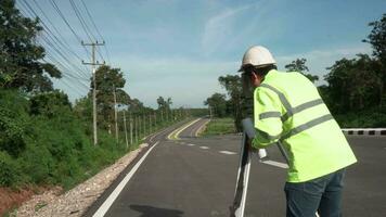 Surveyor engineer with theodolite on road highway during the sunny day with road in background. video