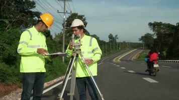 Zusammenarbeit von Landvermesser Ingenieure Arbeiter Herstellung Messung mit Theodolit auf Straße Autobahn. Umfrage Ingenieur beim Straße Konstruktion Grundstück, Landvermesser Ausrüstung. Konstruktion Konzept. video