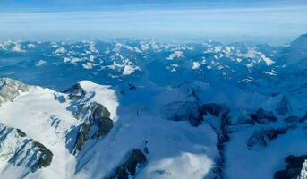 ai generado aéreo ver de Alpes montaña rango con nieve y azul cielo. foto