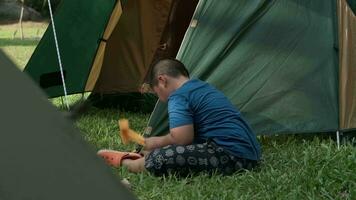 Aziatisch jongen installeren een camping tent in een buitenshuis plaats. video