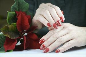 young female hands with beautiful winter manicure design, red color with white snowflakes, Christmas decor photo