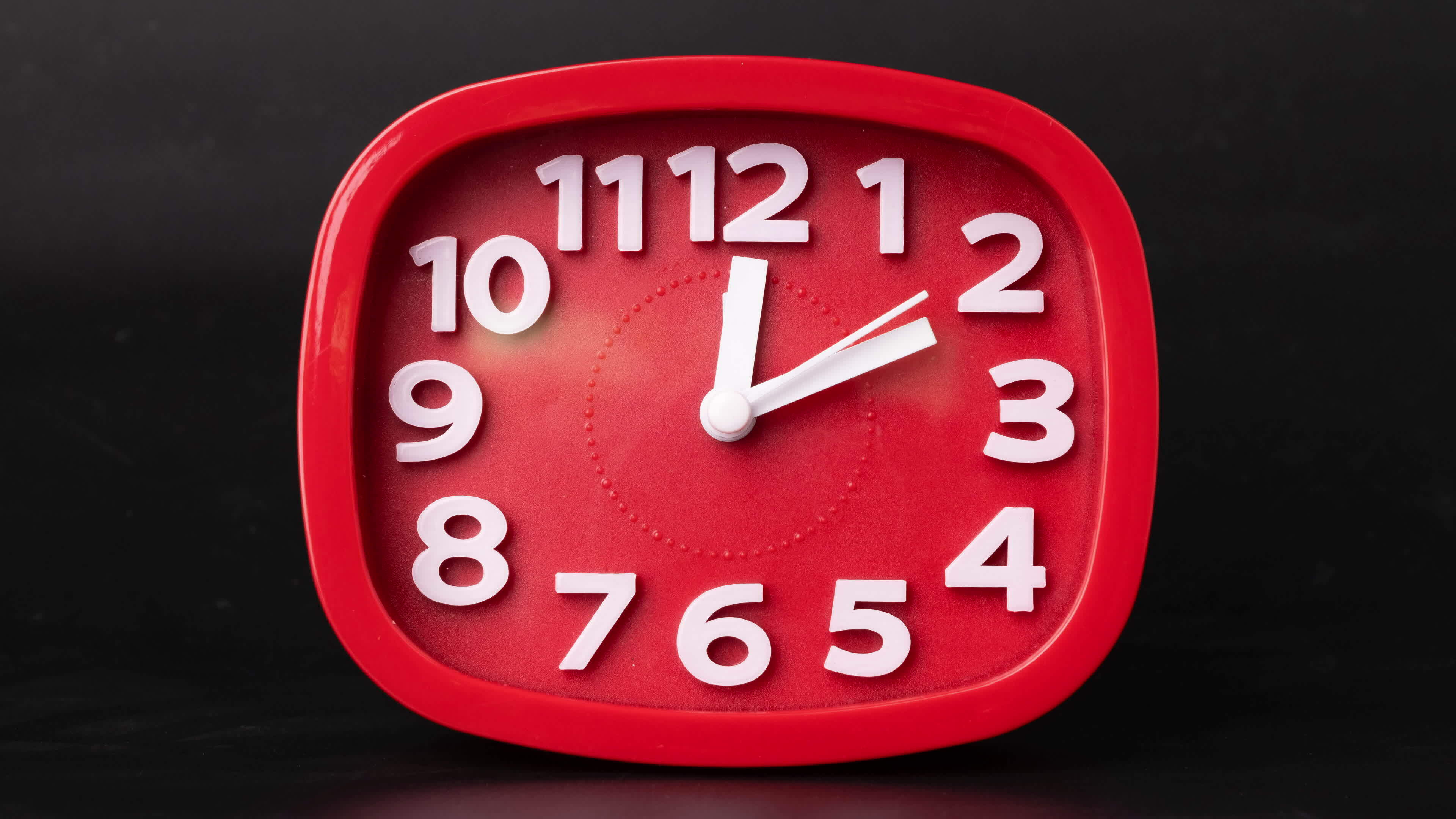 Closeup of red clock time lapse on black background. A red wall clock