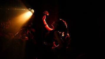 The silhouette of a female dancer holding jewelry in the dark of night is lit by the light of a burning fire photo