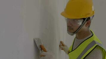Asian construction worker,spatula in hand against the background of a white wall, work plasterer. Putty walls with their own hands. video