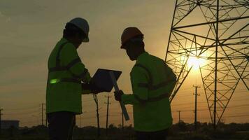 Aziatisch manager bouwkunde in standaard- veiligheid uniform werken inspecteren de elektriciteit hoog Spanning pool met tablet in de buurt toren met elektriciteit. video