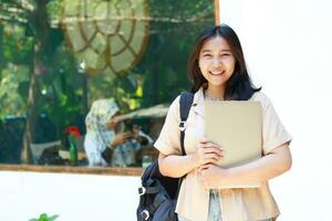 smiling asian woman standing in front of coffee shop bring laptop and backpack wearing stylish casual clothes, female small business owner photo