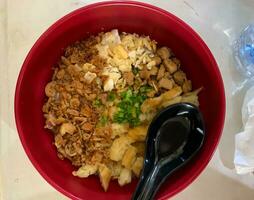 closeup bubur ayam or chicken rice porridge in red bowl with black spoon and topping, top view photo