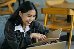 happy asian woman reading notebook and using laptop in library to studying photo