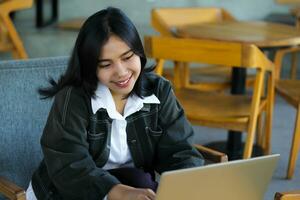 cheerful asian woman typing on laptop working remote from cafe photo