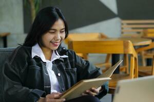 happy asian woman reading notebook and using laptop in library to studying photo