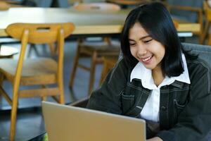 cheerful asian woman typing on laptop working remote from cafe photo