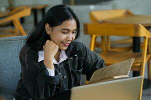 happy asian woman reading notebook and using laptop in library to studying photo