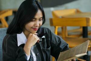 happy asian woman reading notebook and using laptop in library to studying photo