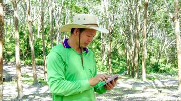 Asian rubber farmer  checking quality of rubber liquid by tablet technology  from  rubber plantation ,technology agricultural rubber product Concept. photo