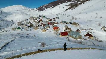 aéreo zangão Visão do uma só caminhante admirando uma montanha Vila durante inverno. neve branco panorama e alpinista estilo de vida. video