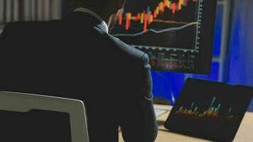 Businessman analyzing a graphic of a stock exchange chart. Back of the head of a young male businessman looking at a stock diagram on the big screen of the computer video