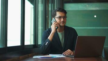 Young asian man talking phone and work from cafe with laptop computer. photo