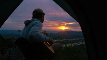 POV past tent young man playing guitar waking up at sunrise. photo