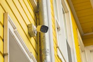 CCTV security camera operating on yellow color wooden building photo
