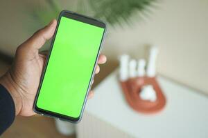 holding smart phone with green screen and home interior decoration on table photo