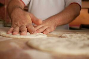 the chef's hands form a round pizza base from the dough with his hands. photo