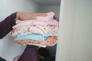 Woman storing a baby's clothes in the drawer of a white wardrobe. photo