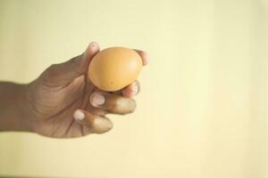 close up of men hand holding a egg against orange color background photo