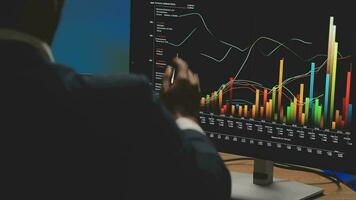 Businessman analyzing a graphic of a stock exchange chart. Back of the head of a young male businessman looking at a stock diagram on the big screen of the computer video