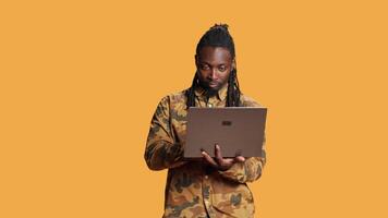 African american guy looks at information on laptop, searching for something on online webpages using portable computer. Young person in studio holding pc and looking at network sites. video