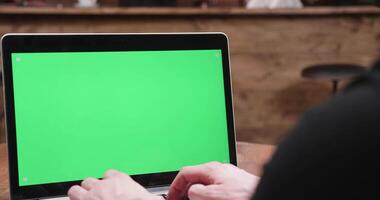 homme les types vite sur une ordinateur avec vert écran sur afficher dans une ancien en bois café video