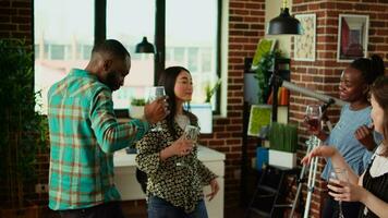 BIPOC group of young adults dancing at apartment party while drinking wine glasses. Friends hanging around house, busting dance moves to rhythmic music in stylish living room video