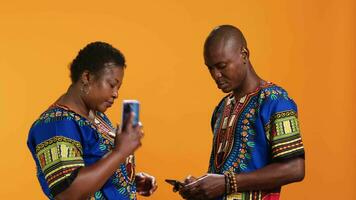 Cheerful couple talking to family on phone call, having remote conversation with smartphone over orange background. Young people in traditional clothes chatting on telephone line. video