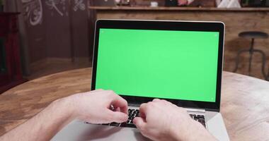 Parallax POV footage of male hands working on computer with green screen. In the backgorund - a cozy and hipster vintage coffee shop video