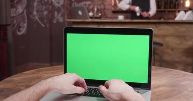 parallax pov schot van persoon typen Aan de laptop met groen scherm Aan. in de achtergrond - een knus wijnoogst cafe video