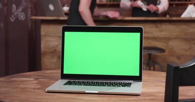 ordenador portátil con verde pantalla en el monitor en acogedor cafetería. un cliente es hablando a el barman en el antecedentes video