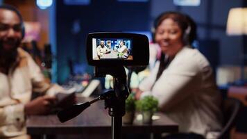 Focus on professional camera used to record radio show presenter live conversation with man in personal studio. Close up on production gear with host and guest talking in blurry background video