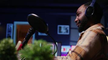 Close up of BIPOC man talking with woman, streaming podcast using vlogging camera during live political debate on vlog channel. Host in dimly lit studio filming internet show, panning shot video