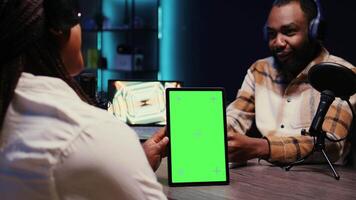 Online show host holding green screen tablet while listening to guest opinion on current events during live broadcast for social media platforms. Mockup device used by influencer recording podcast video