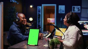 isolé écran tablette suivant à vlogger spectacle hôte bavardage avec client dans néon lumières fleuri vivant pièce studio. chrominance clé dispositif sur table avec homme et femme séance et discuter sur Podcast video