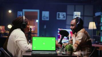 Green screen laptop next to woman laughing during comedy focused podcast, entertained by funny man. Mockup notebook near talking show interviewer telling jokes to audience watching at home video