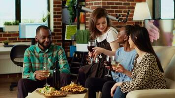 Portrait of happy friends having entertaining conversation, eating snacks from charcuterie board at home. Cheerful african american, asian and caucasian people throwing party in cozy apartment video