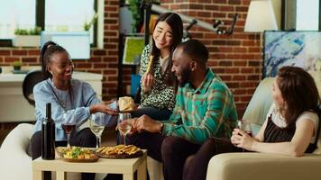 Multiracial friends throwing surprise birthday party forafrican american man, giving him thoughtful gift in living room. Smiling group of people celebrating host anniversary, gifting nice present video