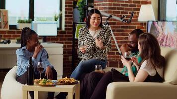 Asian woman discussing with diverse apartment party guests during weekend gathering, making them laugh with hilarious story. Multiracial group of people listening to host making jokes video