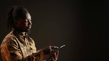 Model holding mobile tablet to check websites over black background, using device to browse through social media pages and connect with his friends. African american man on internet network. video